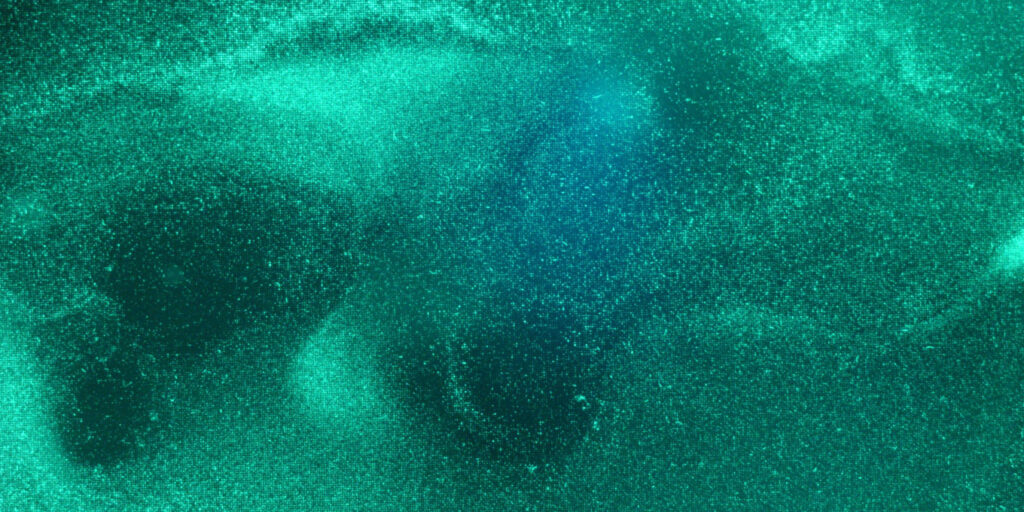 Decorative image by F. Falk, KIT, called "Fluorescent bacteria in microcavities" showing greenish-blue structures seeming to move like a gel-like substance.
