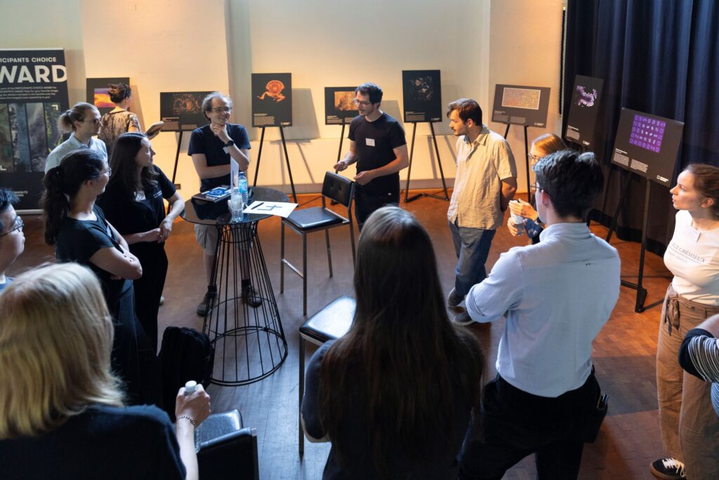 Group of Helmholtz Imaging Conference participants standing in a circle, discussing; in the background the 2025 Best Scientific Image Contest is on display