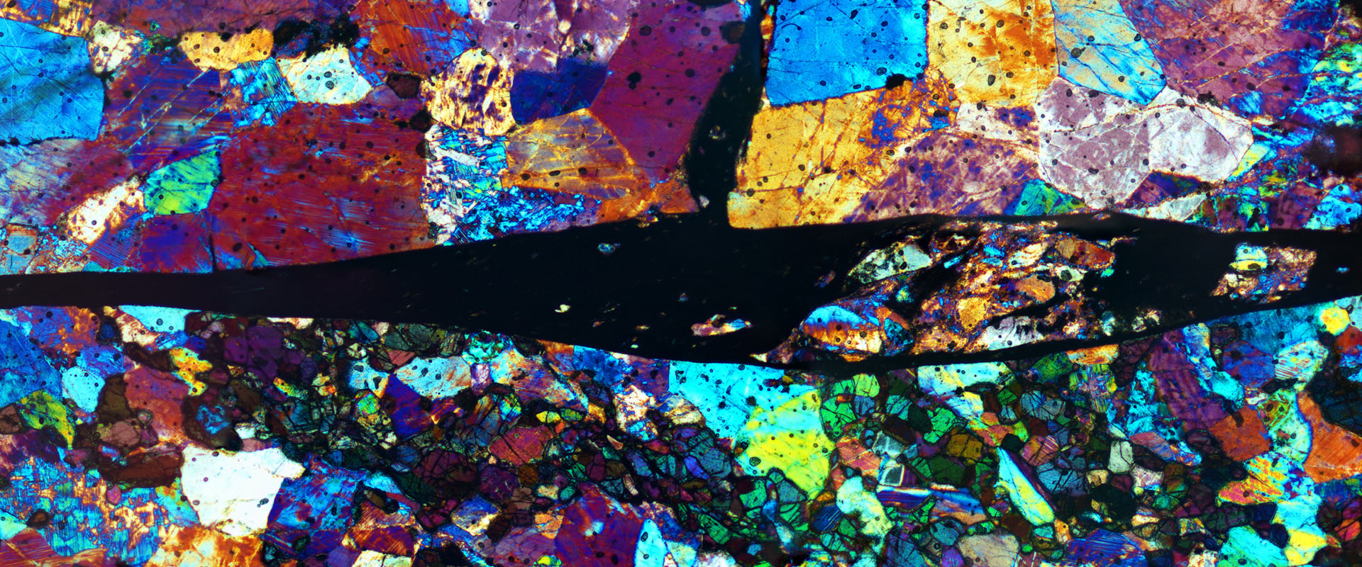 This image shows colorful fragments, the horizontal part in the middle is black. This dark vein is a fossilized earthquake containing rock glass and fragments from the adjacent wall rock.