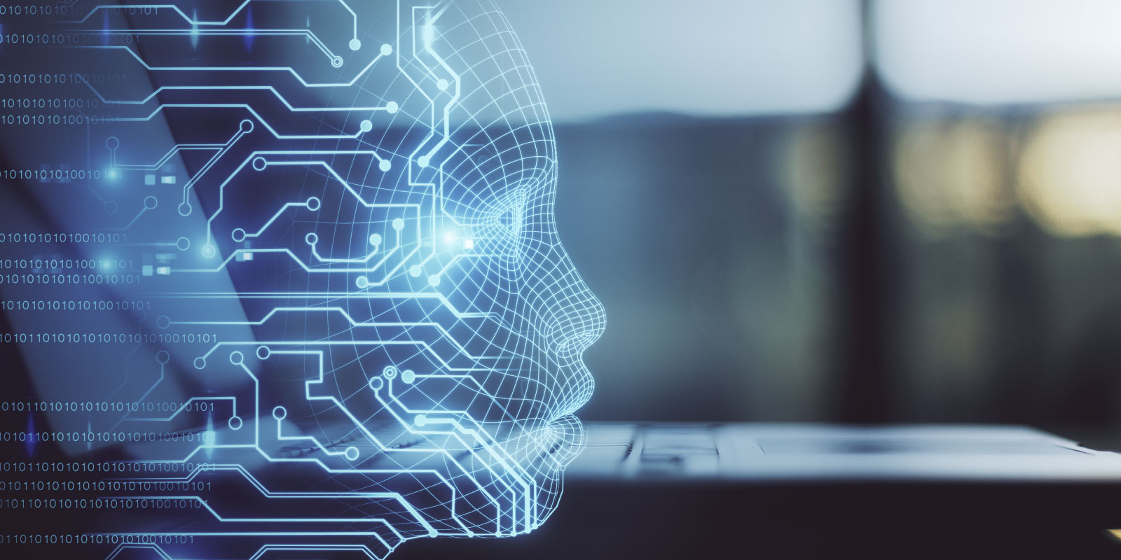 A side profile of a human head formed by glowing blue lines and circuit-like patterns, suggesting a digital or artificial intelligence representation. The face appears semi-transparent and geometric, with interconnected nodes and pathways extending outward. Binary code is faintly visible on the left side, while a blurred laptop sits in the background, reinforcing a technology-focused setting.