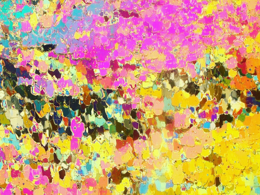 This image resembles an abstract mosaic or painting. It is composed of many irregular, crystal-like shapes in vivid shades of pink, yellow, turquoise, orange, blue, and black. The fragmented patterns create a textured appearance similar to stained glass or cracked ice illuminated by polarized light. What you can see here is a longitudinal thin section of a sea ice core. It has the size of approximal 8 cm x 8 cm. This thin section is made out of a 7-8 mm thick slice of an ice core form the Arctic sea ice, glued with water on a glass plate and processed by a microtome to a very thin layer of < 1 mm. To make the crystal structure of the individual sea ice crystals visible, the glass plate is illuminated with polarized light. Here we see a typical pattern for the so-called granular ice. That means the ice has grown under “rough”, maybe windy, conditions. The knowledge of the crystal structure of the sea ice is important to better understand and to model the light transition through the sea ice into the ocean, which is, for example, of relevance for the phytoplankton growth in the Arctic Ocean.
