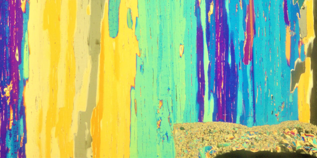 This image shows long vertical streaks in bright yellow, turquoise, blue, and purple. The layered colors and textured lines resemble dripping paint or weathered wood grain, creating a vivid, striped pattern across the image.