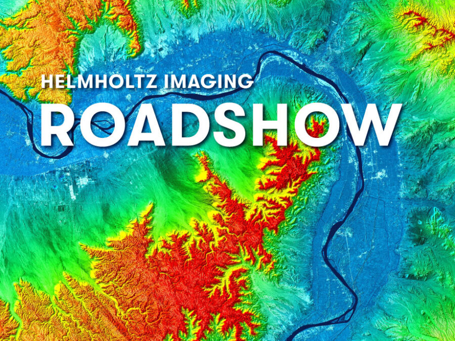Promotional banner for the Helmholtz Imaging Roadshow featuring a color-coded elevation map with mountains, valleys, and a river. Large white text reading “Helmholtz Imaging Roadshow” is displayed over the map, with white corner markers framing the composition.