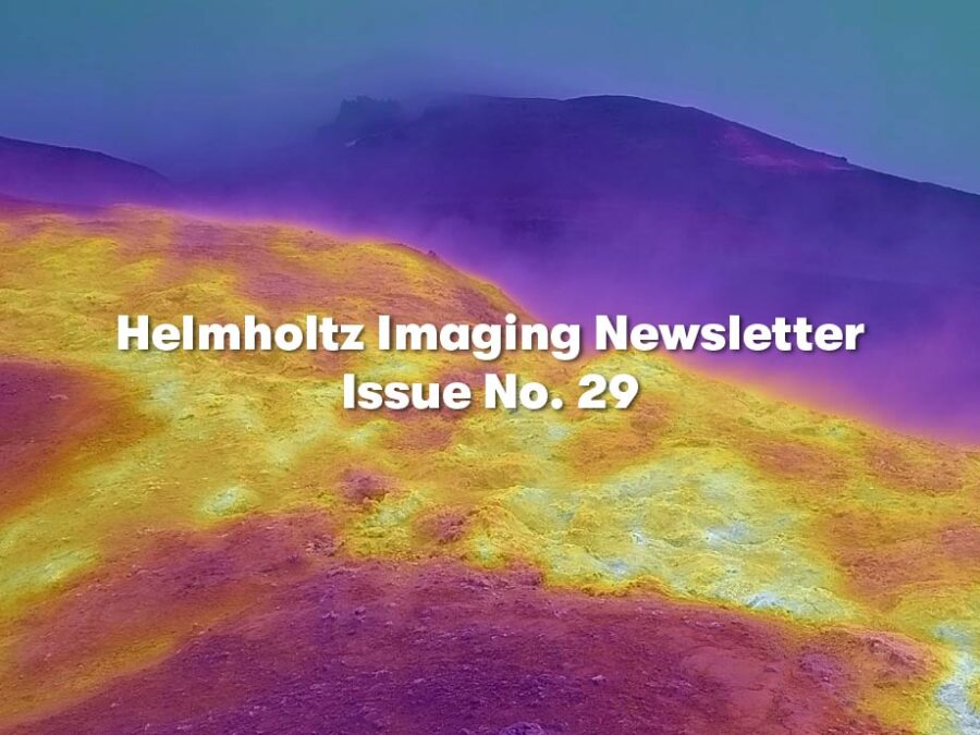 Landscape image showing an undulating, rocky terrain in vivid yellow, orange, pink, and purple tones. A broad yellow-orange area stretches across the center, bordered by purple hills in the foreground and a dark purple ridge beneath a blue sky in the background.